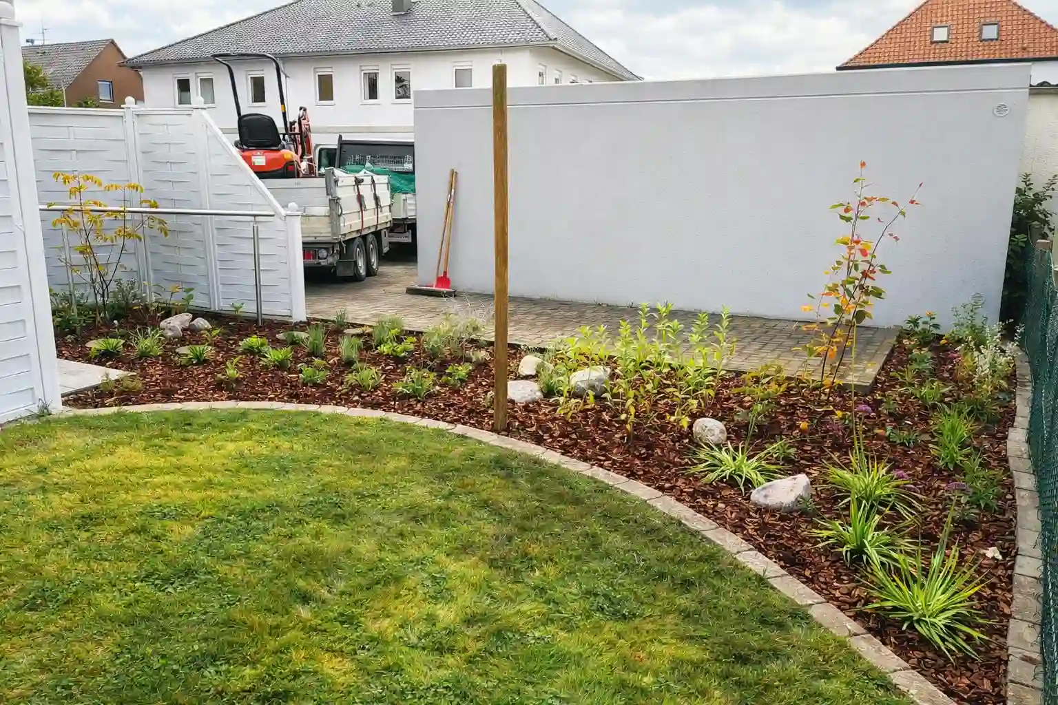 Frisch angelegte Rasenfläche mit neu bepflanztem Beet und Rindenmulch